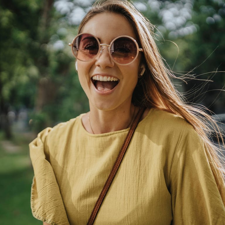 Frau mit Sonnenbrille lacht glücklich.  (Foto: IMAGO, IMAGO / Westend61)