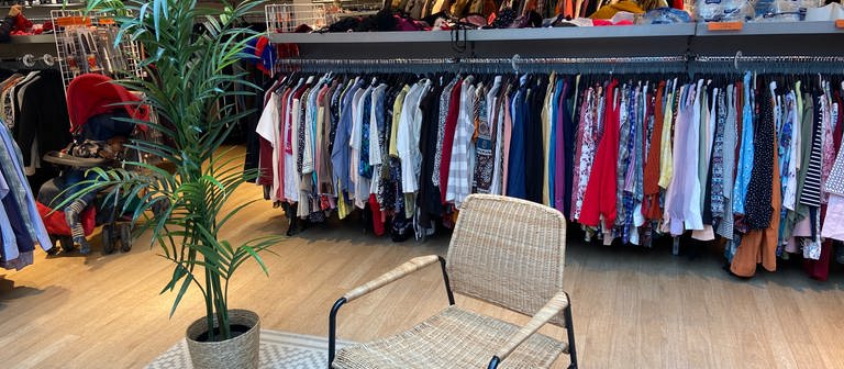 In einem Vintage-Laden in Mannheim hängen zahlreiche Hemden und Oberteile an einer Stange. Im Hintergrund sind Koffer zu sehen.  (Foto: DASDING)