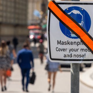 Ein Schild, dass auf die Maskenpflicht hinweist, ist mit Klebeband durchgestrichen. (Foto: dpa Bildfunk, picture alliance/dpa | Peter Kneffel)