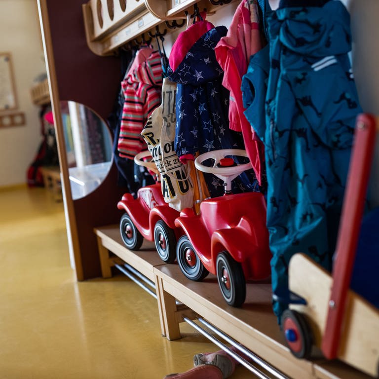 Bobbycars stehen unter Jacken von Kindern, die an einer Garderobe einer Kindertagesstätte (Kita) hängen.  (Foto: dpa Bildfunk, picture alliance/dpa | Philipp von Ditfurth)