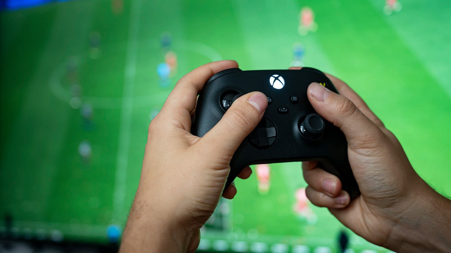 Ein Mann hält einen Xbox-Controller von Microsoft vor einem Fernseher in der Hand.