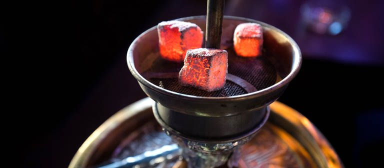 Glühende Kohle liegt auf einem Metallsieb über dem Tabak im Kopf einer Wasserpfeife in einer Shisha-Bar. (Foto: dpa Bildfunk, picture alliance/dpa | Christian Charisius)