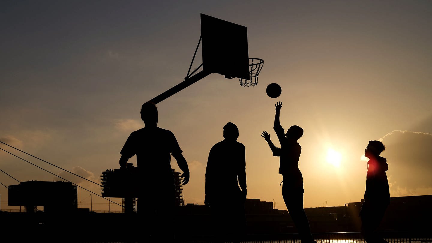 Jugendliche spielen in der Abendsonne am Rheinufer Basketball.
