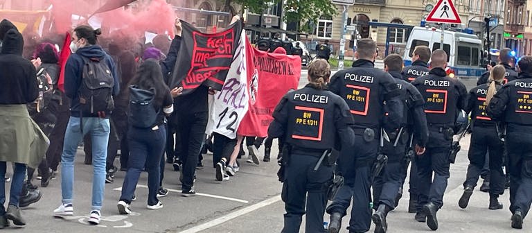 Demonstrierende mit unterschiedlichen Bannern gehen auf der einen Seite, Polizeibeamte auf der anderen Seite in der Innenstadt von Heidelberg. (Foto: SWR)