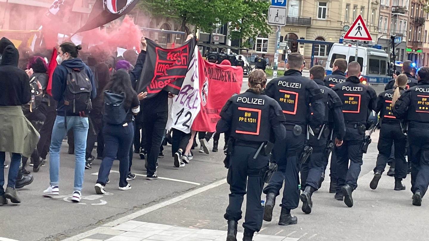 Demonstrierende mit unterschiedlichen Bannern gehen auf der einen Seite, Polizeibeamte auf der anderen Seite in der Innenstadt von Heidelberg.