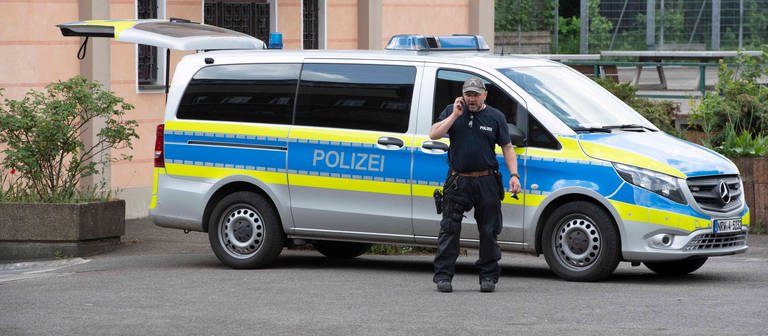 Ein Polizist steht vor einem Polizeiwagen, der vor einer Schule in Essen geparkt wurde. (Foto: IMAGO, IMAGO / Sven Simon)