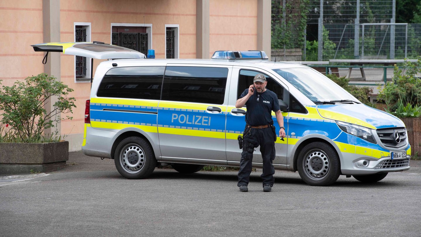 Ein Polizist steht vor einem Polizeiwagen, der vor einer Schule in Essen geparkt wurde.