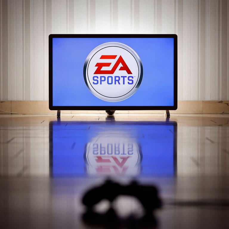 Das Logo der Marke EA Sports des US-amerikanischen Videospielentwicklers und -publishers Electronic Arts auf einem Bildschirm, im Vordergrund ein Gaming-Controller (Foto: imago images, IMAGO / Future Image)