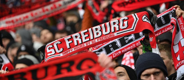 Ein Fan hält einen Schal vom SC Freiburg in die Höhe (Foto: IMAGO, IMAGO / Sven Simon)