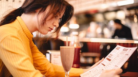 Teenage girl reading menu while sitting in restaurant (Foto: IMAGO, IMAGO / Cavan Images)