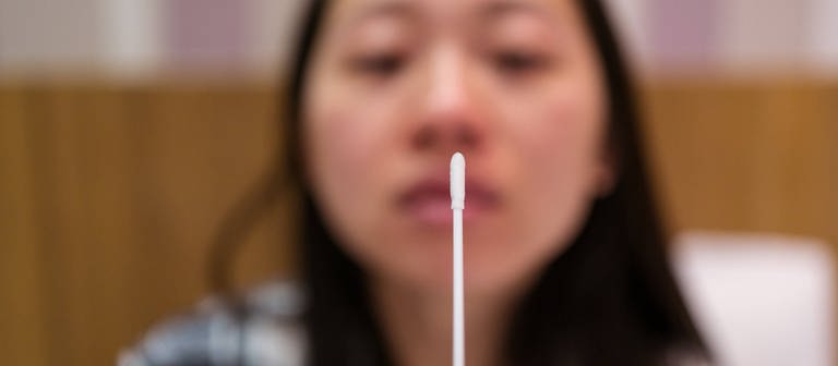 Young Asian female with nasal cotton swab making antigen express test in light hotel room during quarantine and coronavirus pandemic (Foto: IMAGO, IMAGO / Addictive Stock)