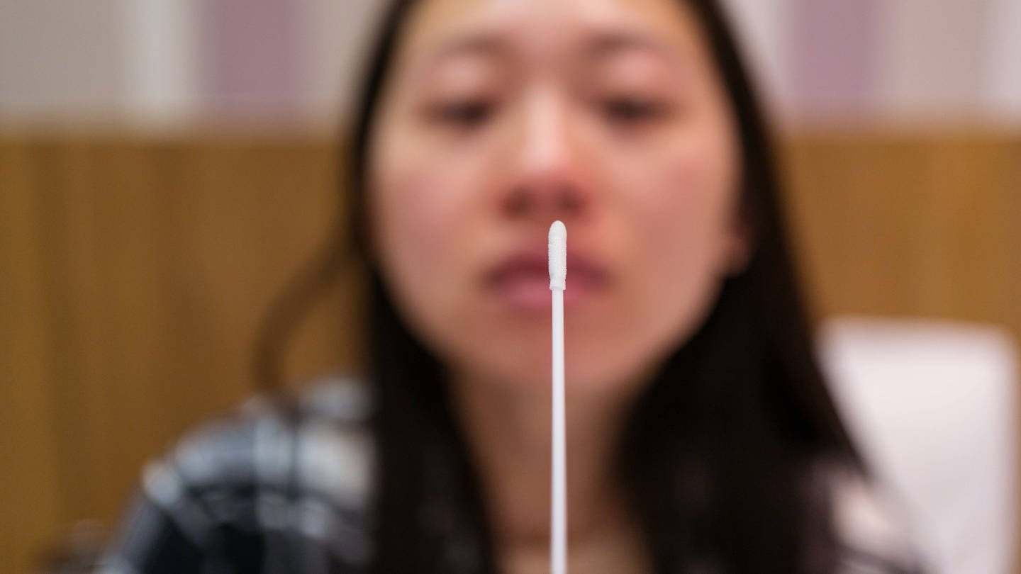 Young Asian female with nasal cotton swab making antigen express test in light hotel room during quarantine and coronavirus pandemic