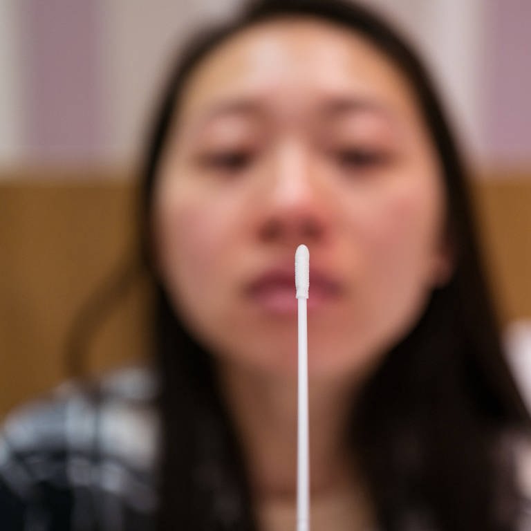 Young Asian female with nasal cotton swab making antigen express test in light hotel room during quarantine and coronavirus pandemic (Foto: IMAGO, IMAGO / Addictive Stock)
