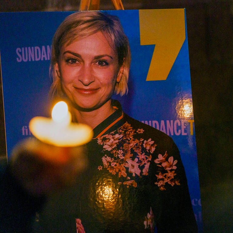 Ein Foto von der Kamerafrau Halyna Hutchins. Menschen sitzen mit Kerzen daneben und trauern (Foto: IMAGO, IMAGO / ZUMA Wire)