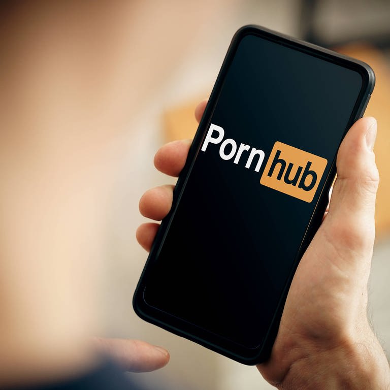 Eine Hand hält ein Handy. Auf dem Bildschirm ist das Logo von "Pornhub" zu sehen. (Foto: IMAGO, IMAGO / Bihlmayerfotografie)