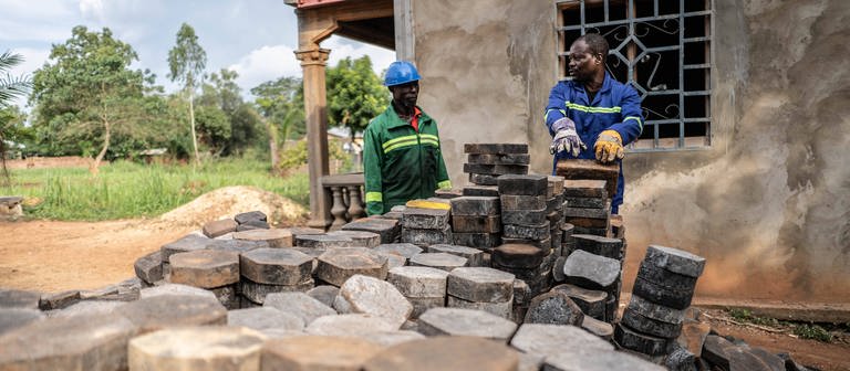Zwei Männer stehen hinter Pflastersteinen, die aus recyceltem Plastik hergestellt wurden in Bangui in der Zentralafrikanischen Republik. (Foto: IMAGO, IMAGO / Xinhua)