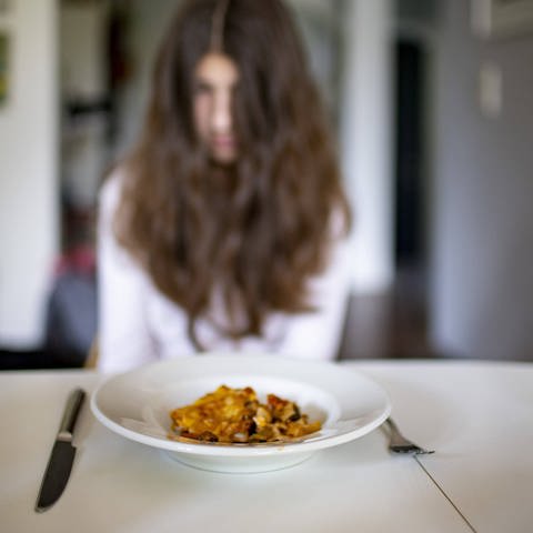 Mädchen sitzt vor Teller mit Essen - Magersucht hat in der Corona-Pandemie zugenommen. (Foto: IMAGO, IMAGO / photothek)