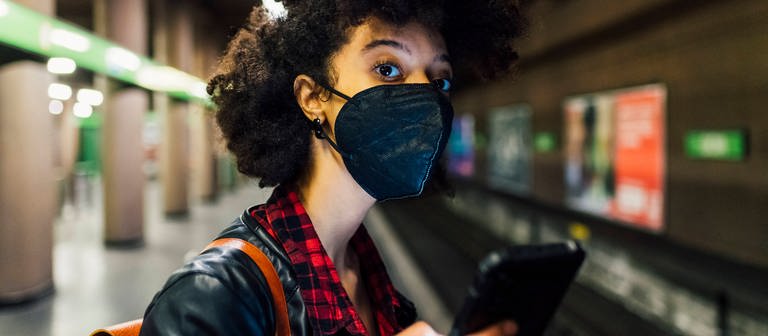 Young woman with protective face mask holding mobile phone at subway model released Symbolfoto (Foto: DASDING, IMAGO, IMAGO / Westend61)