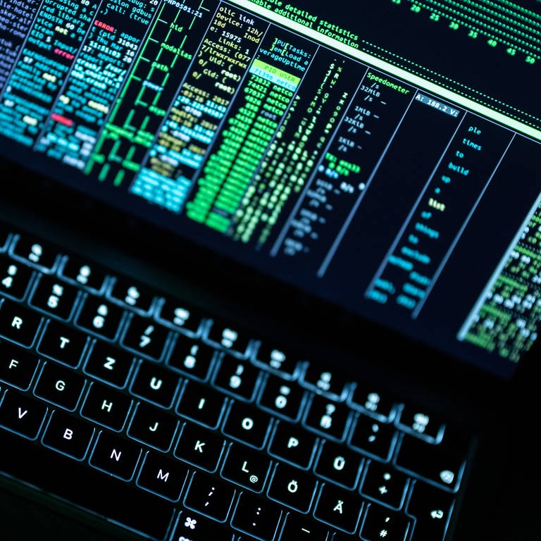 Auf einem Notebook mit beleuchteter Tatstatur wird auf dem Display sehr viel Programmiercode angezeigt. (Foto: IMAGO, IMAGO / Silas Stein)