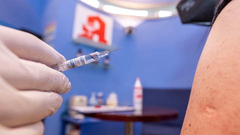 Archivbild: Eine Spritze mit Grippe-Impfstoff wird in Richtung eines freien Oberarms gehalten. Dahinter ist ein Apotheken-Logo zu sehen. (Foto: dpa Bildfunk, picture alliance/dpa | David Inderlied)