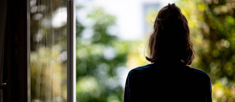 Eine Frau steht in ihrer Wohnung an einem Fenster. (Foto: dpa Bildfunk, picture alliance/dpa | Fabian Sommer)