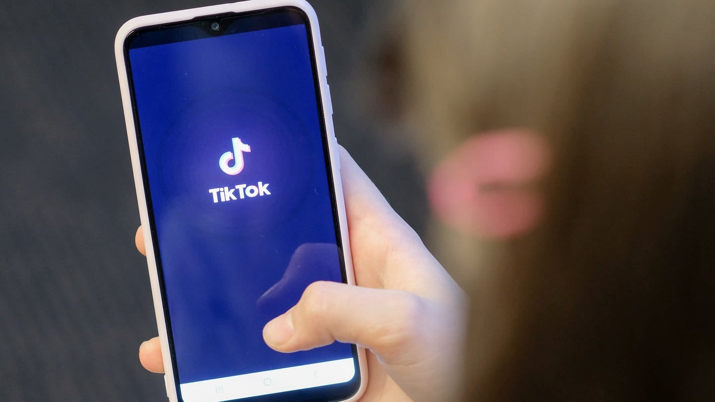 Ein Mädchen hält ihr Smartphone in den Händen, auf dem das Logo der Kurzvideo-App TikTok zu sehen ist. (Foto: dpa Bildfunk, picture alliance/dpa/dpa-Zentralbild | Jens Kalaene)