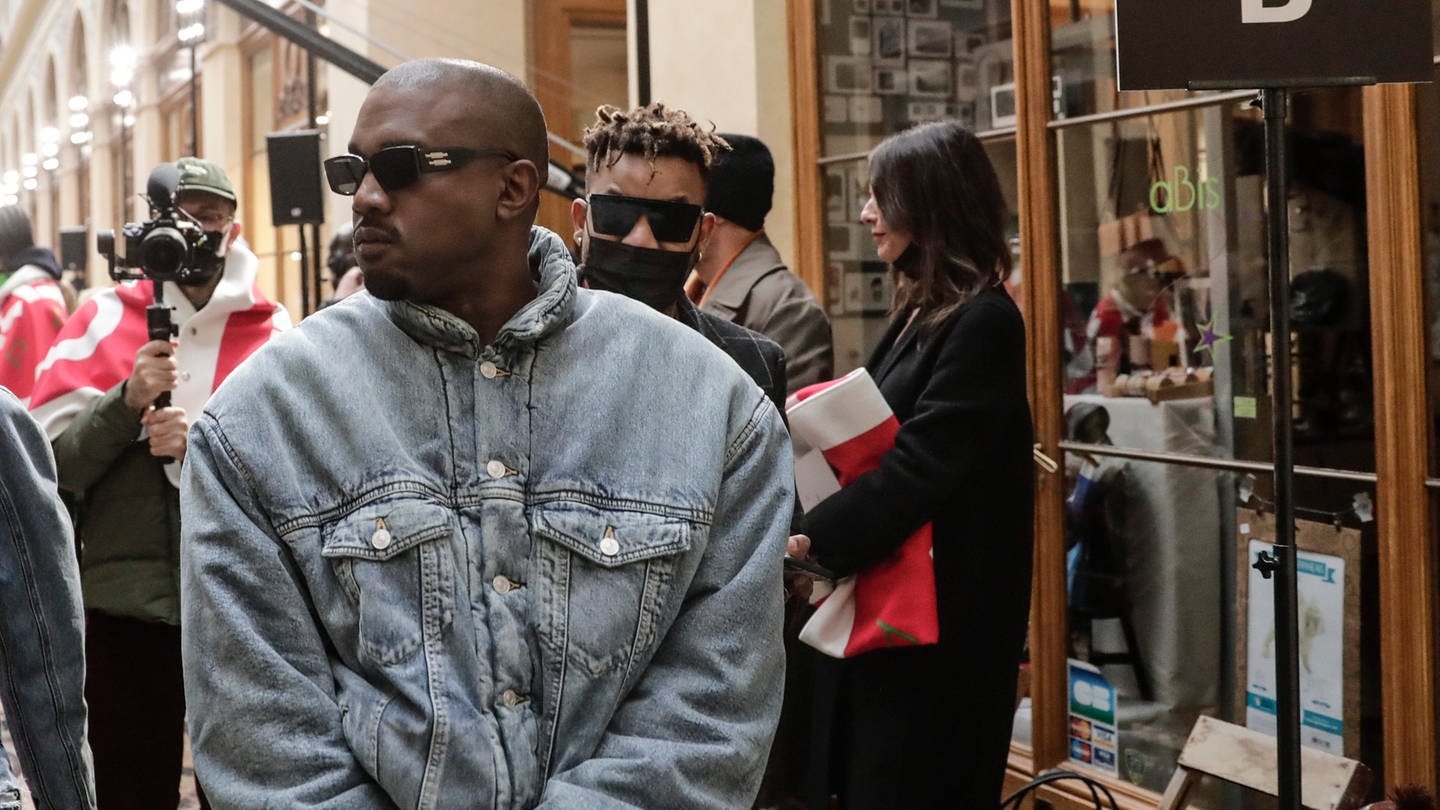Kanye West in Jeansjacke und mit Sonnenbrille, gefolgt von seiner Freundin und Kameraleuten (Foto: dpa Bildfunk, picture alliance/dpa/AP | Lewis Joly)