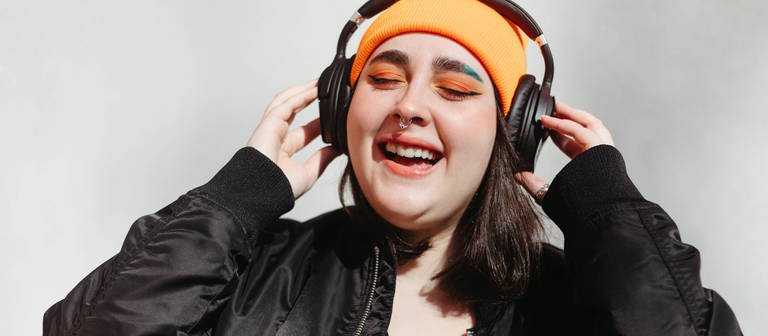 Eine Frau hört mit Kopfhörer Musik und singt dabei. (Foto: IMAGO, IMAGO / Addictive Stock)