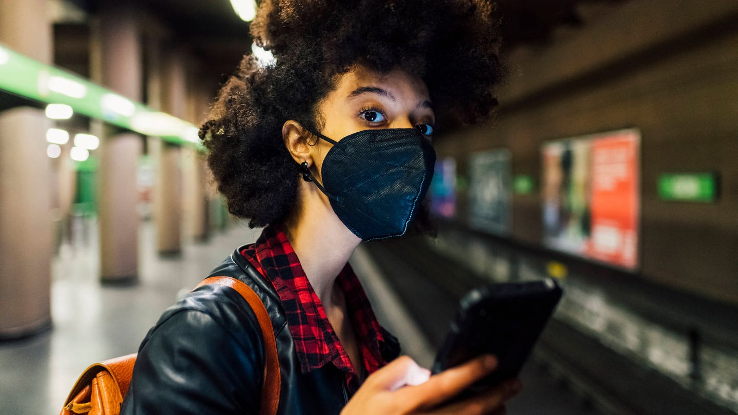 Young woman with protective face mask holding mobile phone at subway model released Symbolfoto