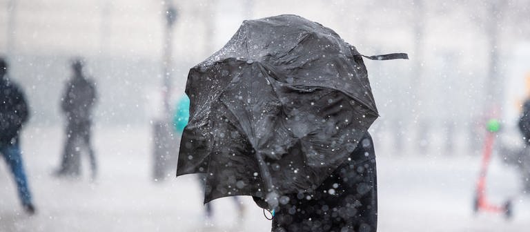 Ein Mann steht mit einem Regenschirm bei Schneegestöber  (Foto: dpa Bildfunk, picture alliance/dpa | Christophe Gateau)