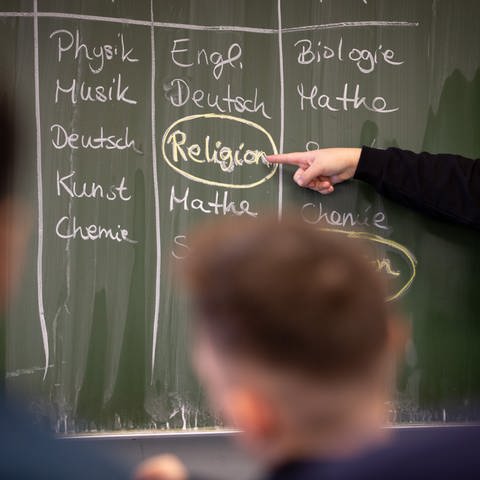Schülerin Delin steht an einer Tafel, auf der ein Stundenplan mit Religionsunterricht geschrieben ist. (Foto: dpa Bildfunk, picture alliance/dpa | Friso Gentsch)