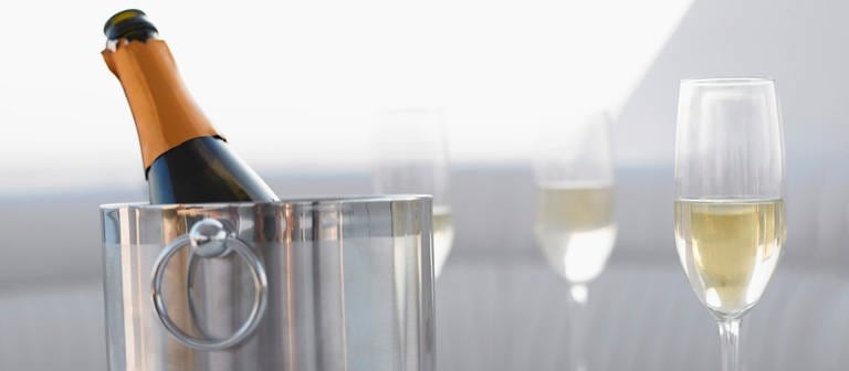 Eine Champagner-Flasche steht in einem Kühlbehälter auf einem Tisch neben zwei gefüllten Gläsern. (Foto: IMAGO, IMAGO / YAY Images)