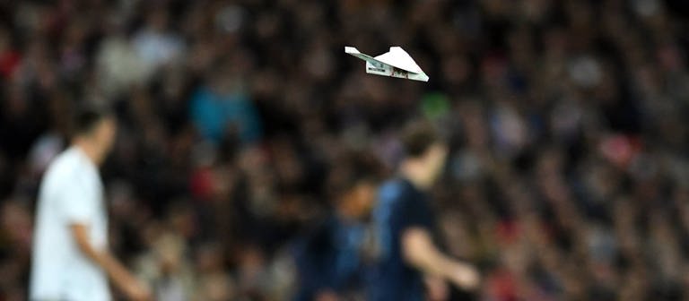 Ein Papierflieger fliegt über das Spielfeld. (Foto: IMAGO, IMAGO / Revierfoto)