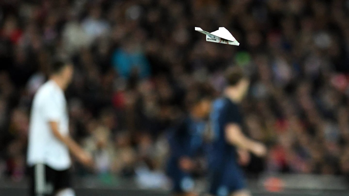 Ein Papierflieger fliegt über das Spielfeld.
