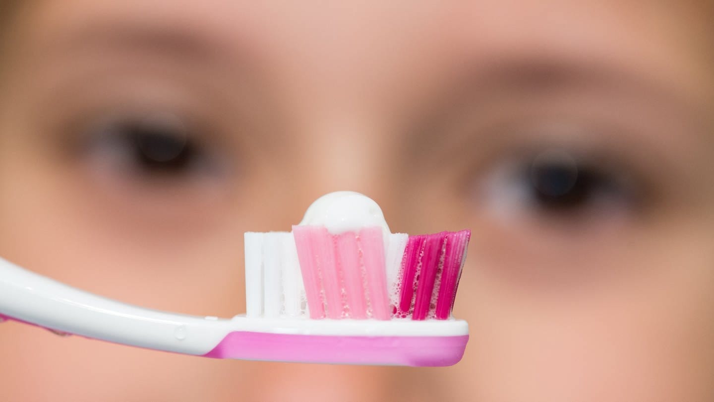 Zahnbürste mit Zahnpasta - im Hintergrund ein Gesicht