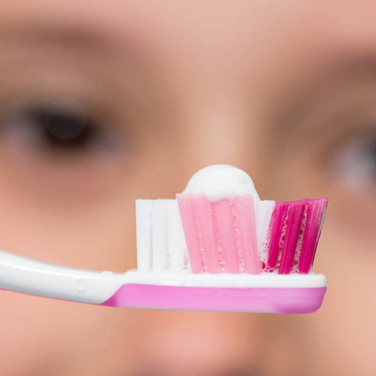 Zahnbürste mit Zahnpasta - im Hintergrund ein Gesicht (Foto: dpa Bildfunk, picture alliance / dpa | Patrick Seeger)