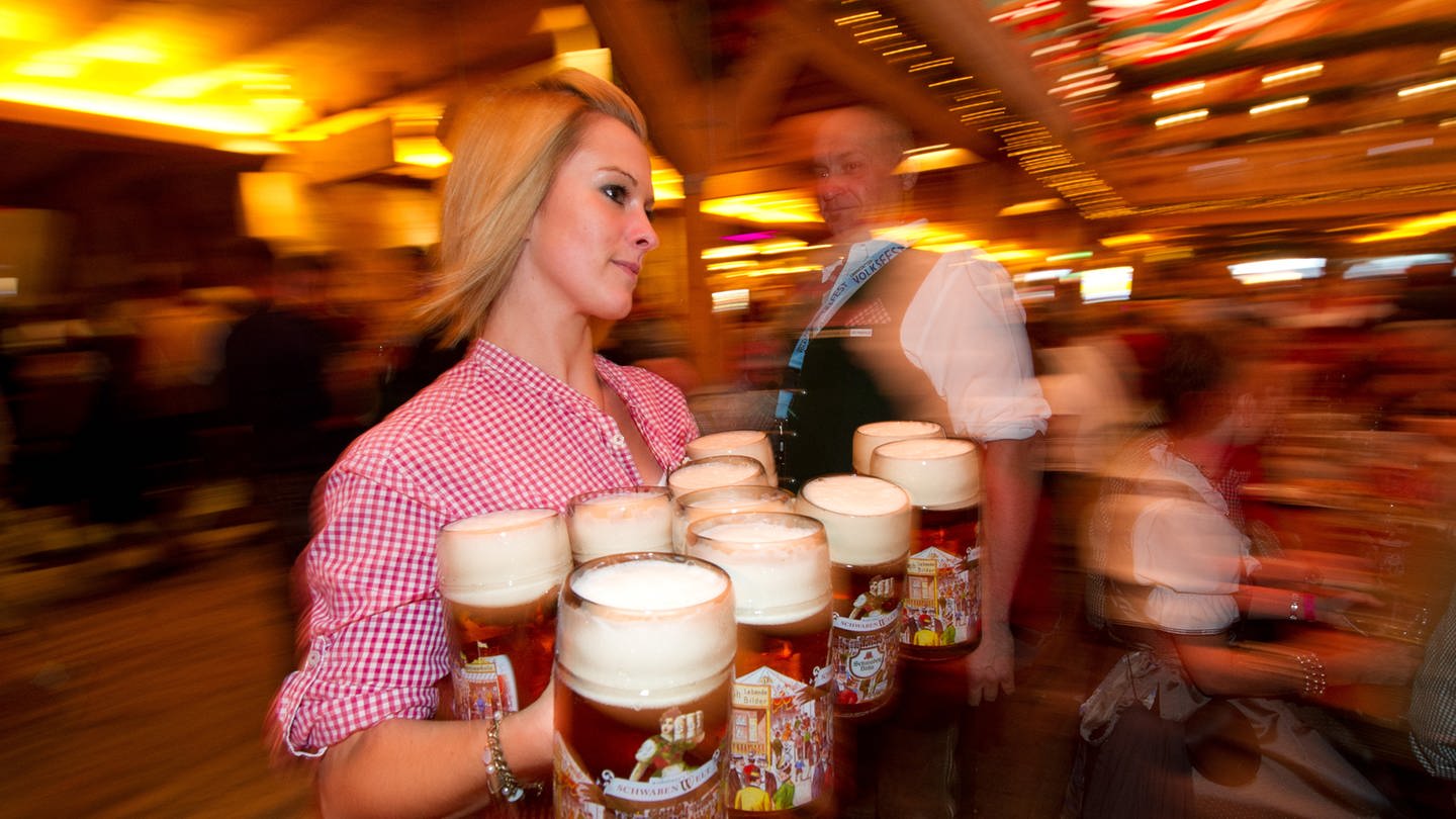 Eine Frau trägt zehn Bierkrüge in den Händen.