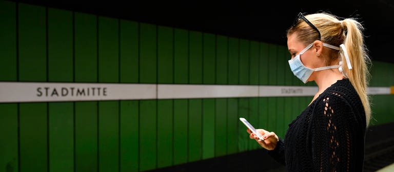 Frau mit Mundschutzmaske, am Handy, wartet auf Zug (Foto: IMAGO, IMAGO / Michael Weber)