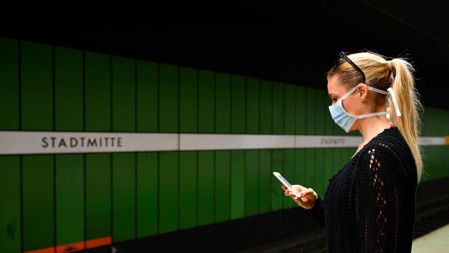 Frau mit Mundschutzmaske, am Handy, wartet auf Zug (Foto: IMAGO, IMAGO / Michael Weber)