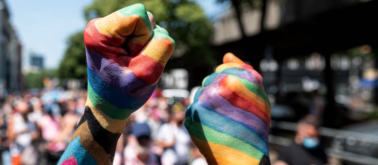 Zwei Teilnehmer der «Pride Berlin: Save our Community, Save our Pride» halten ihre Faust in die Höhe, die in Regenbogenfarbe angemalt sind. (Foto: dpa Bildfunk, picture alliance/dpa | Fabian Sommer)