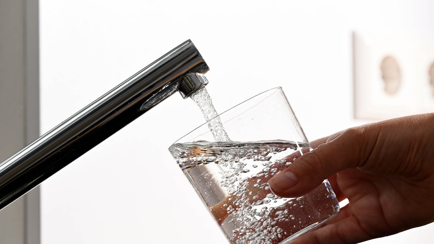 Eine Hand hält ein Wasserglas unter einen Wasserhahn