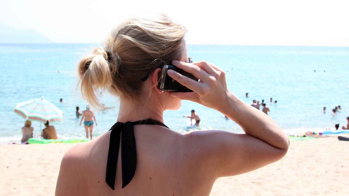 Eine Frau steht mit Handy am Strand.