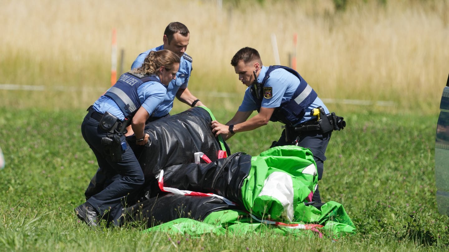 Polizeibeamte transportieren die Hülle einer Hüpfburg ab. Das Spielgerät war bei einem Fest auf dem Sportplatz von Gondershausen von einer Windböe erfasst.