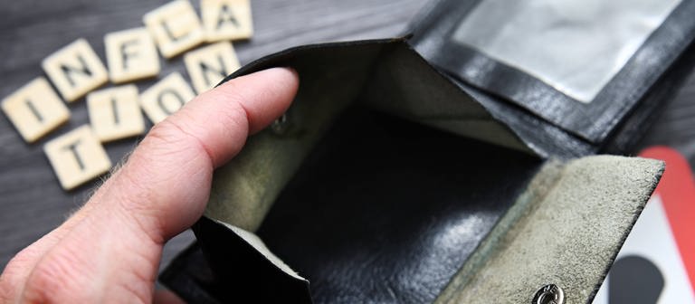 Hand öffnet leeres Portemonnaie, Schriftzug Inflation und Gefahrenschild. (Foto: IMAGO, IMAGO / Christian Ohde)
