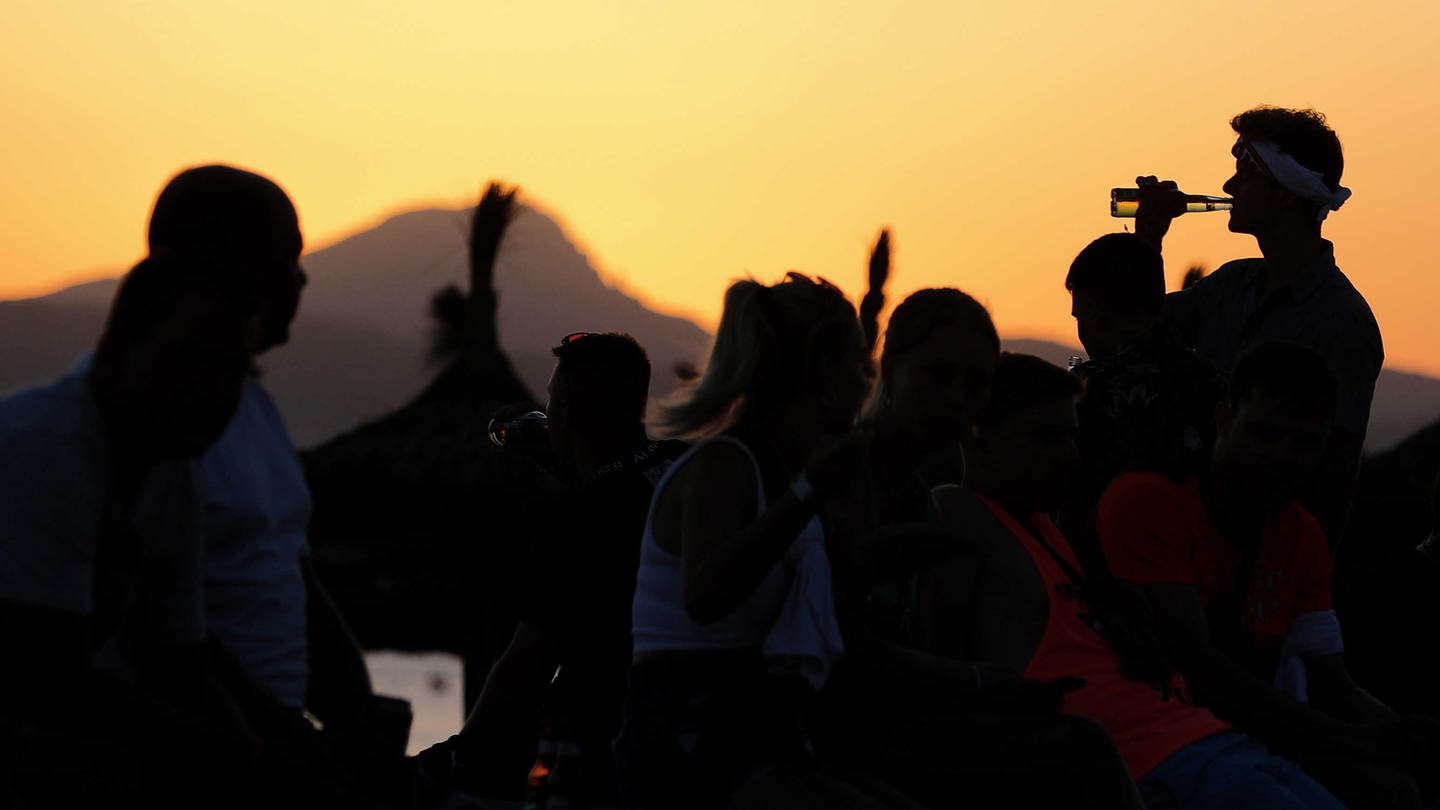 Junge Leute feiern bei Sonnenuntergang am Strand von Arenal am Party-Viertel Ballermann auf Mallorca.