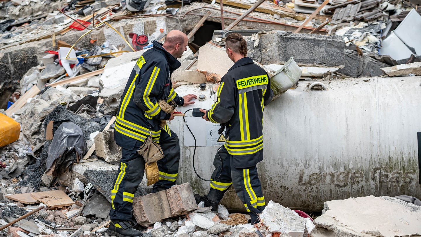 Feuerwehrleute machen eine Messung an einem Gastank zwischen den Trümmern.