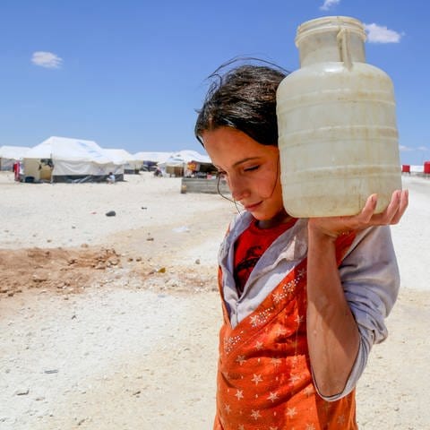 Eine junge Frau trägt in einem Flüchtlingscamp in Syrien eine Wasserflasche. (Foto: dpa Bildfunk, picture alliance / Souleiman/Unicef/Syria 2017/dpa | Souleiman)