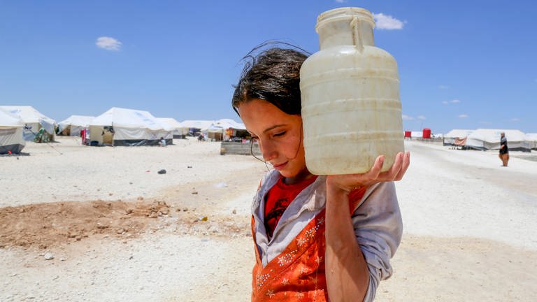 Eine junge Frau trägt in einem Flüchtlingscamp in Syrien eine Wasserflasche. (Foto: dpa Bildfunk, picture alliance / Souleiman/Unicef/Syria 2017/dpa | Souleiman)