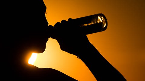 Ein junger Mann sitzt biertrinkend auf dem Kronsberg, während am Horizont die Sonne untergeht. (Foto: DASDING, picture alliance/dpa | Julian Stratenschulte)
