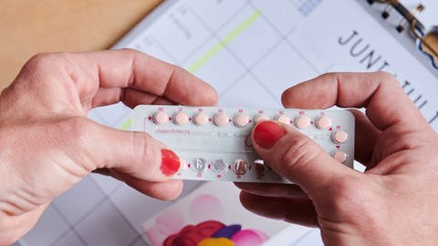 Über einem Kalender nimmt sich eine Frau die nächste Pille aus der Monatspackung der Antibabypille. (Foto: dpa Bildfunk, picture alliance/dpa | Annette Riedl)